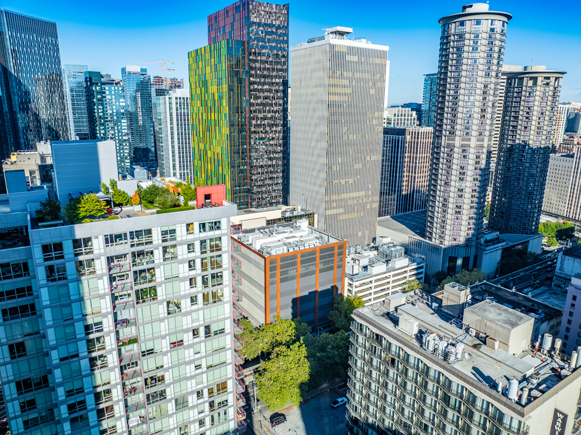 Aerial view of downtown Seattle skyline with modern skyscrapers, including a colorful building with green and yellow panels, against a clear blue sky.